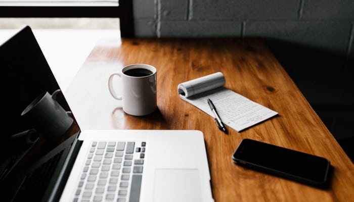 a laptop and writing pad on a desk beside a black smartphone